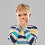 Un niño se tapa la boca porque tiene halitosis