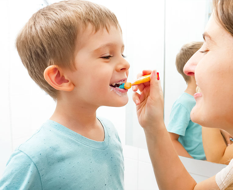 Joven madre cuidadosa cepillando y limpiando los dientes de su pequeño hijo. Padres e hijos cuidando la salud e higiene de los dientes.