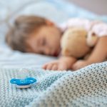 bebé durmiendo con en una cama con un chupete al lado