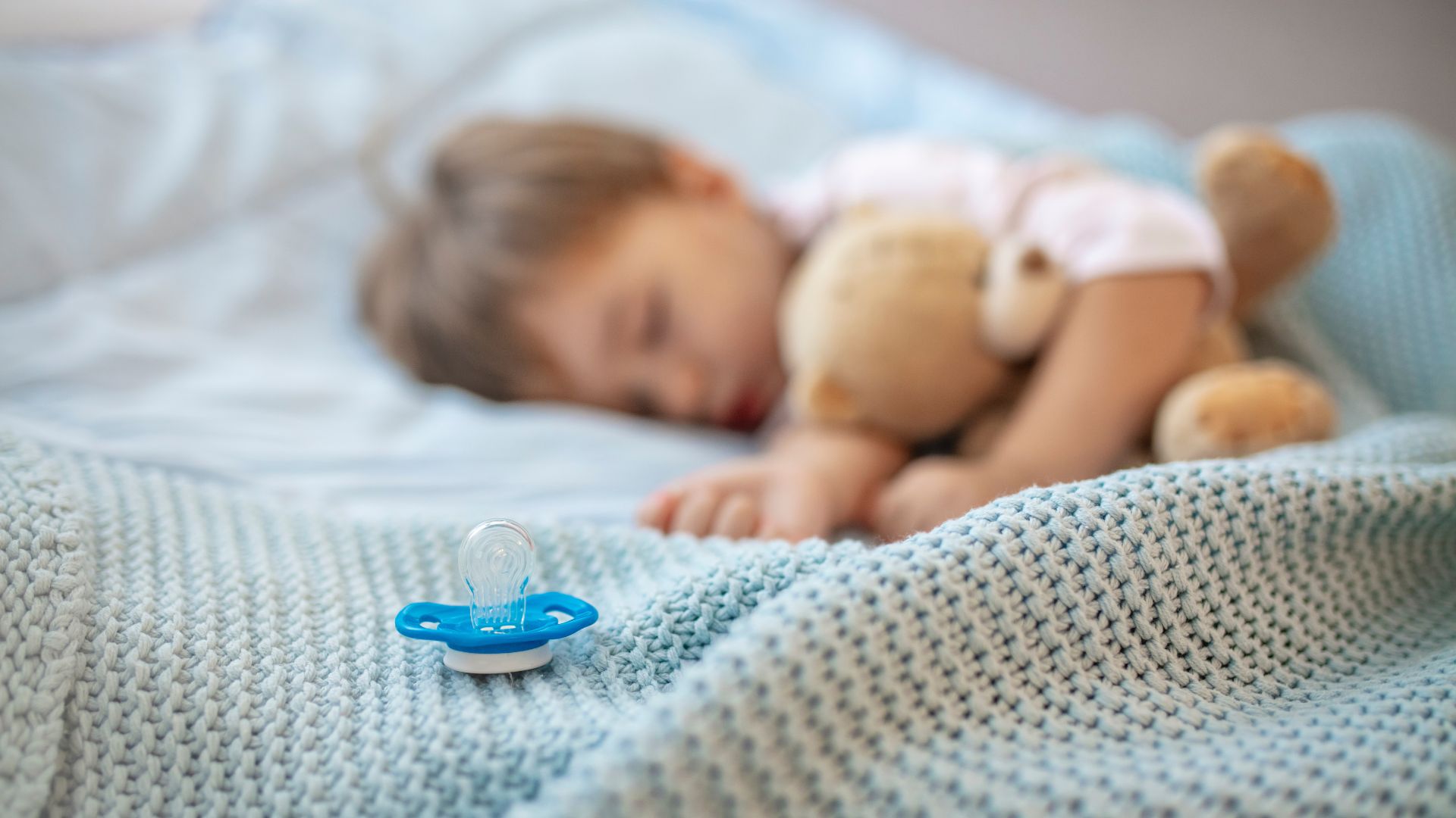 bebé durmiendo con en una cama con un chupete al lado